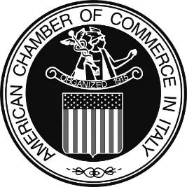 Black and white circular logo of the American Chamber of Commerce in Italy, featuring a figure with a winged staff above a U.S.-style shield, and the text "Organized 1915" in the center.