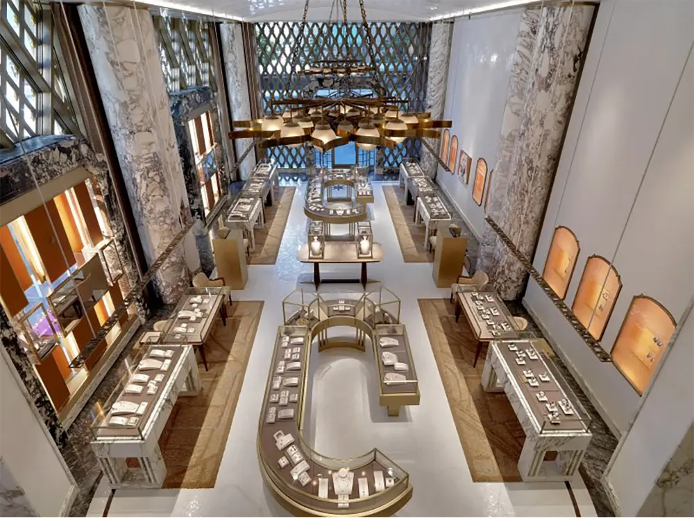 A luxurious jewelry store interior with marble walls, elegant lighting, and multiple display cases showcasing jewelry on white surfaces. The space is spacious, symmetrical, and richly decorated.