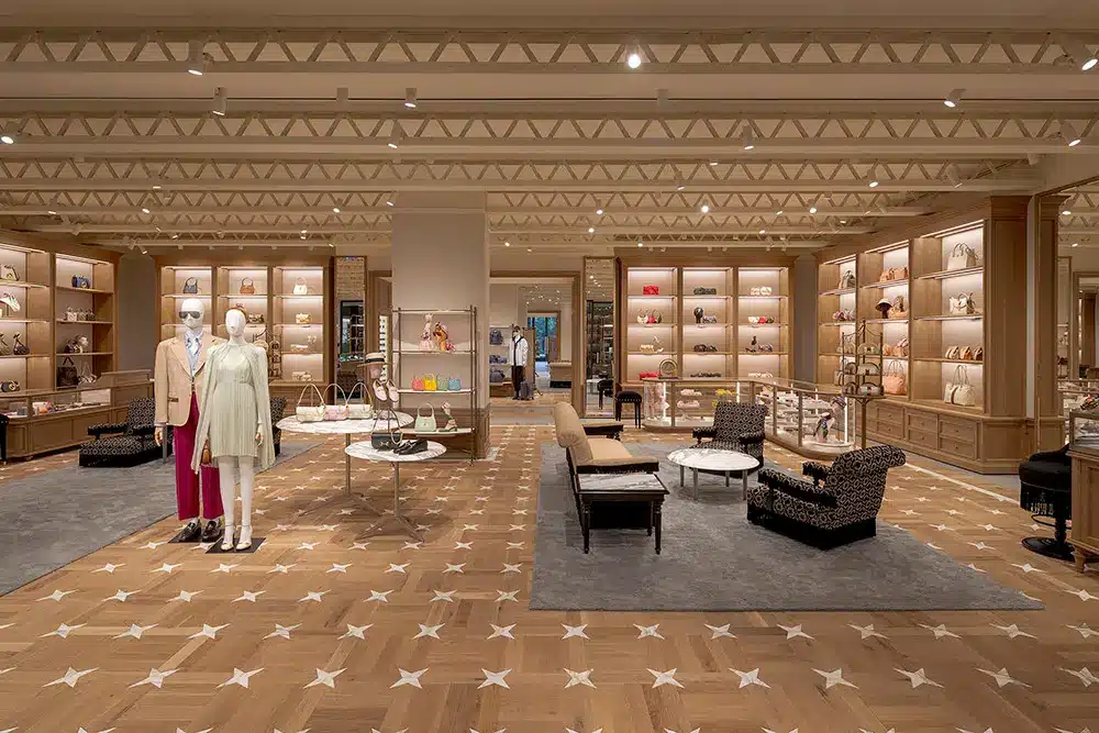 Spacious luxury boutique with mannequins dressed in stylish clothing, shelves displaying handbags and accessories, elegant seating areas, and wooden flooring with star patterns.