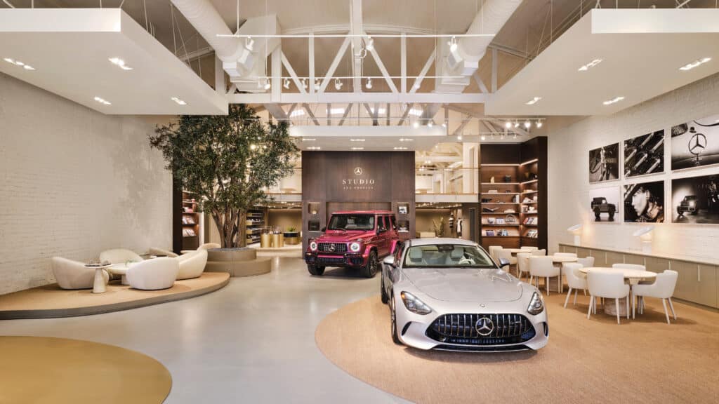 A modern, stylish car showroom with a white sports car and a red SUV on display, surrounded by contemporary seating, wall art, and shelves with merchandise.